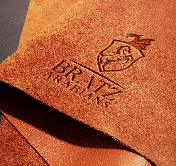 Custom horse logo design for Bratz Arabians engraved on luxurious brown leather, featuring a crest with a rearing horse and dragon motif.