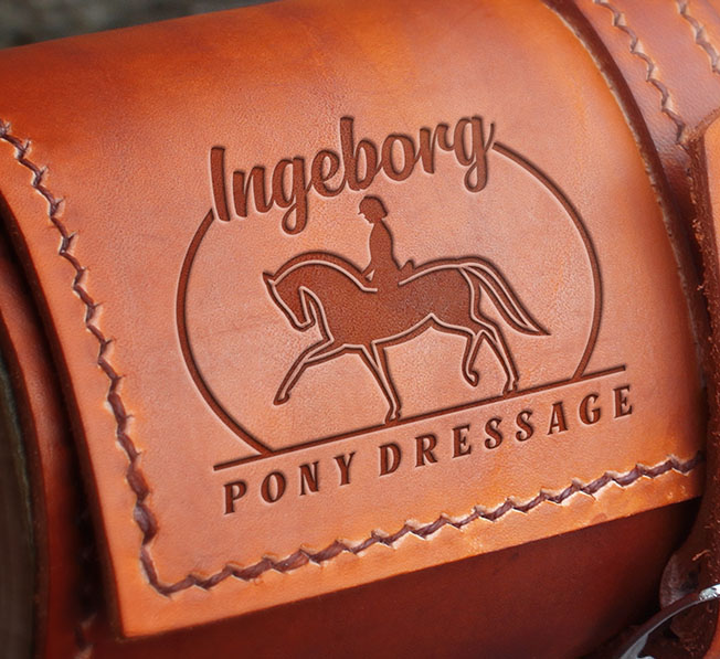 Elegant embossed logo for Ingeborg Pony Dressage featuring a pony and rider silhouette inside a circular frame, displayed on a leather saddle.
